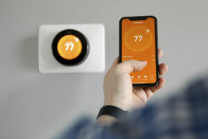Person using smartphone to adjust smart thermostat displaying temperature, illustrating modern home climate control and compatibility with high-efficiency furnaces.