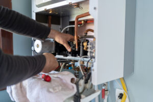 Hands performing maintenance on a boiler, inspecting internal components and connections, highlighting the importance of regular boiler upkeep for efficient heating solutions.